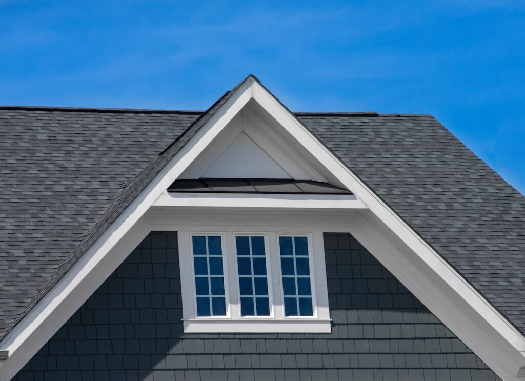 roofing dover oh Attic three pane window on grey blue siding, gable, corbel, louver on a new construction luxury American single family home in the with blue sky background