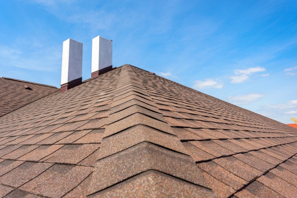 how long does a roof last Photo of new roof with asphalt tile and two white chimney on new home under construction, against blue sky