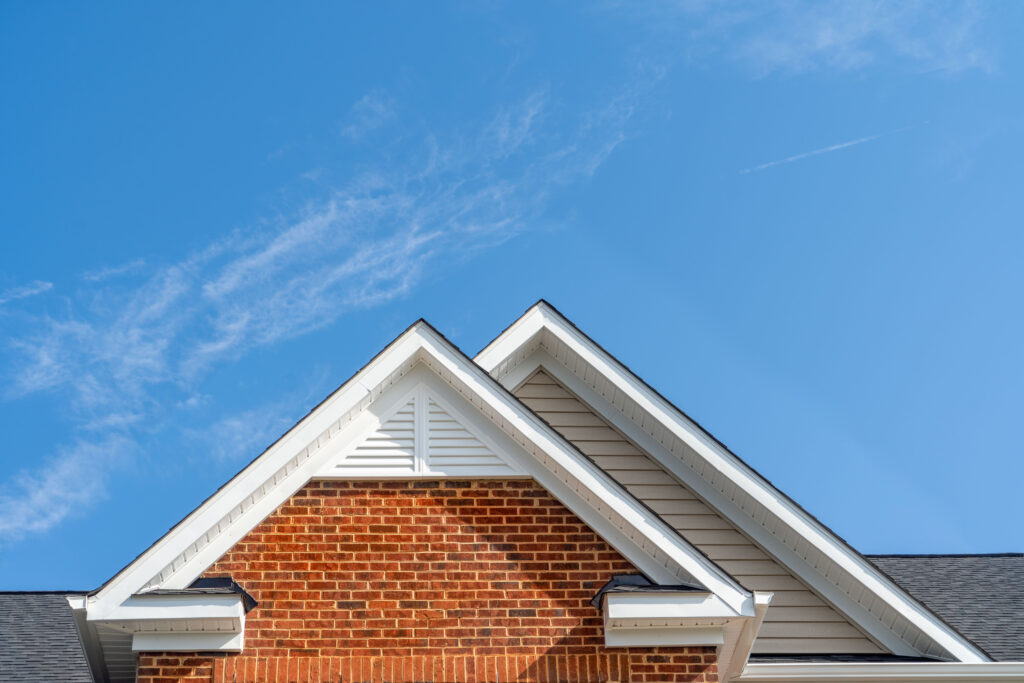 Double gable with beige horizontal vinyl lap and red brick facade siding, with triangle shape white attic vent on a pitched roof attic at an American single family home neighborhood USA