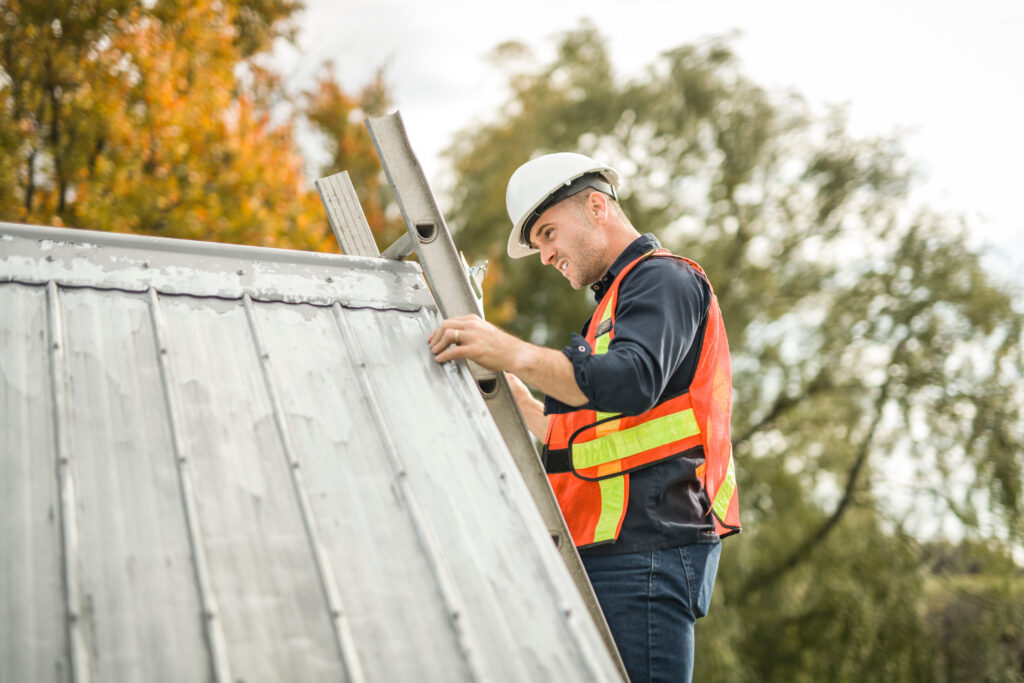 roof inspection cost A man with hard hat standing on steps inspecting house roof