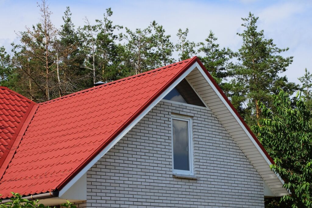 gray brick attic with a window under a red tile roof against the sky and pine trees